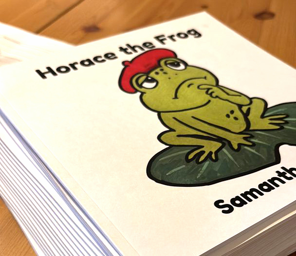 Copies of Horace the Frog stacked on a wooden table